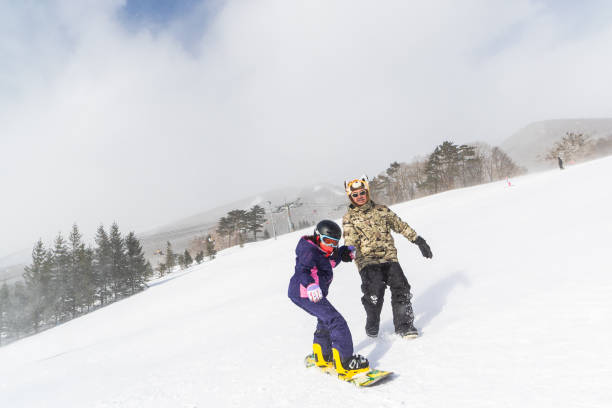 Man teaching young child to snowboard A man teaching a young Japanese girl how to snowboard for the first time. japanese snowboarder stock pictures, royalty-free photos & images