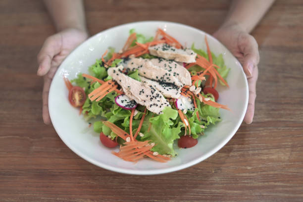 Hand holding a plate of chicken salad on table