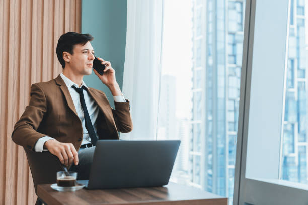istock Businessman talking phone to manager while sitting near window. Ornamented. 1805104033