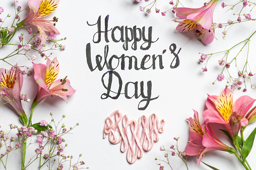 Happy Women's day holiday lettering over white background with beautiful pink Peruvian lily flowers and small purple flowers. Holiday concept
