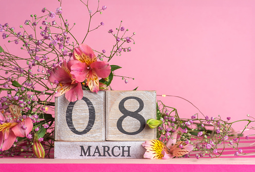 International Women's Day. Beautiful postcard for March 8. Spring pink flowers and Happy Women's Day on light textured wood. Holiday concept on pink background