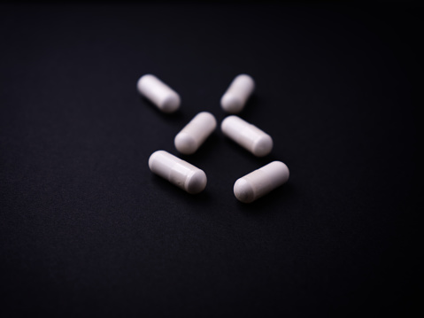 Creatine capsules on dark paper background. Soft focus. Close up. Copy space.