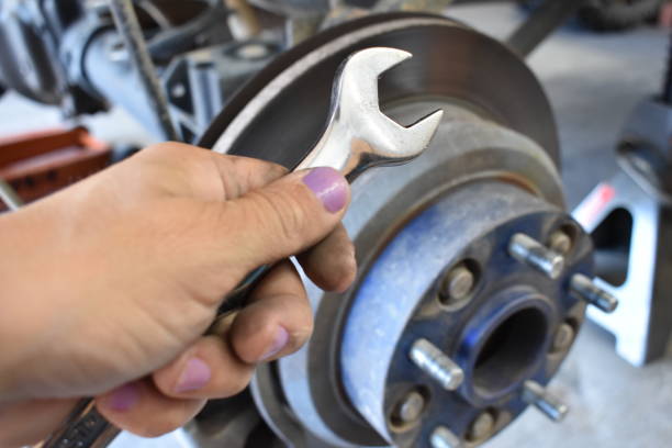 istock Female Hand with Wrench working on Car with Tire Off 1805196694