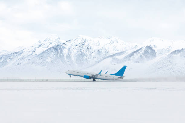 decollo di un aereo passeggeri in una forte tempesta di neve sullo sfondo di alte montagne innevate pittoresche - airfield mountain snow airport foto e immagini stock
