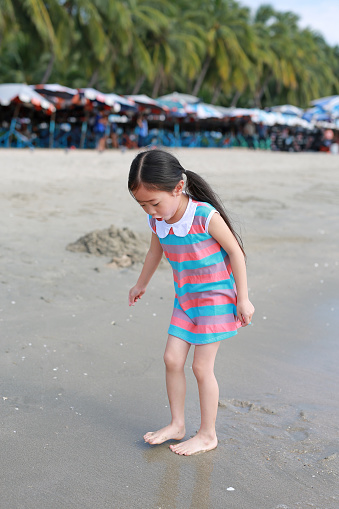 Exciting Asian child girl while come to play sand and sea at the beach on holiday.