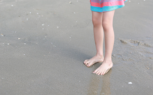 Kid legs in dress standing on sand beach.