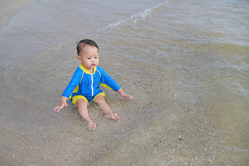 Portrait of Asian baby boy in swimming suit sitting on the sand beach.