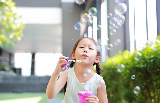 Little Asian girl blowing a soap bubbles in garden outdoor.