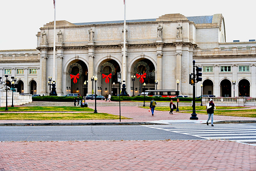 Washington, D.C., USA - November 20, 2023: Christmas wreaths hang from the massive archways at Union Station as pedestrians cross in front of it on a late autumn day.
