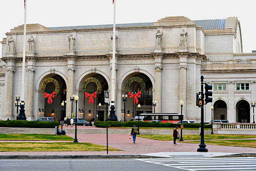 Washington, D.C., USA - November 20, 2023: Christmas wreaths hang from the massive archways at Union Station as pedestrians cross in front of it on a late autumn day.