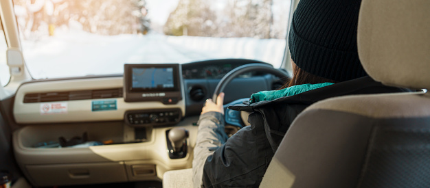 Happy Traveler driving car on snowy road, woman Tourist enjoying snow forest view from the car in winter season. Winter travel, Road trip, Exploring and Vacation concepts