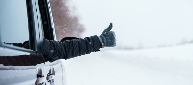 Happy Traveler driving car on snowy road and gesture finger up, man Tourist enjoying snow forest view from the car window in winter season. Winter travel, Road trip, Exploring and Vacation concepts