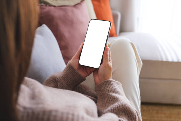 istock Mockup image of a woman holding mobile phone with blank desktop white screen while sitting on a sofa at home 1805263348