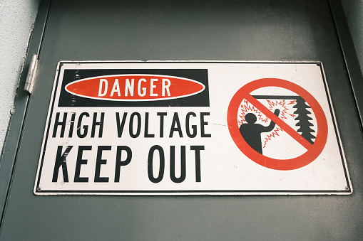 Danger, high voltage, keep out sign on a green door.