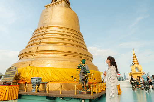 Woman in white outfit exploring Wat Saket in Bangkok  and standing on the background of golden stupa