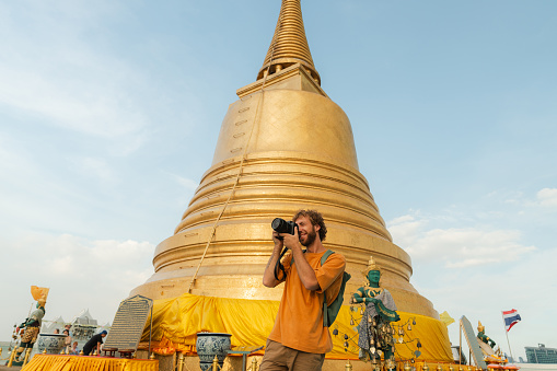 Cheerful man  photographing with camera on the background of Golden stupa in Bangkok