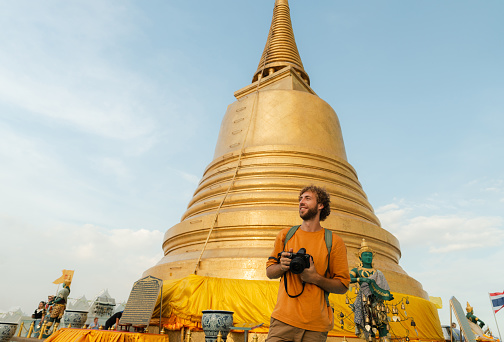Cheerful man  photographing with camera on the background of Golden stupa in Bangkok