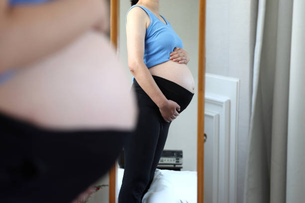 Pregnant woman Pregnant woman looking at her belly in front of a full-length mirror woman full length mirror stock pictures, royalty-free photos & images