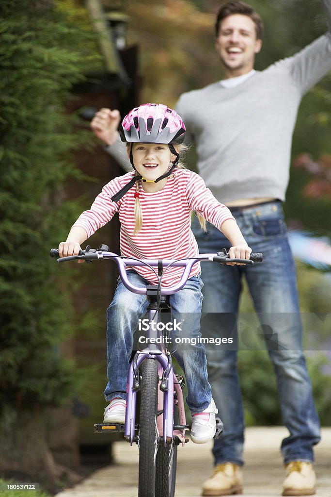 Father Teaching Daughter To Ride Bike In Garden Father Cheering While Teaching Daughter To Ride Bike In Garden 20-29 Years Stock Photo