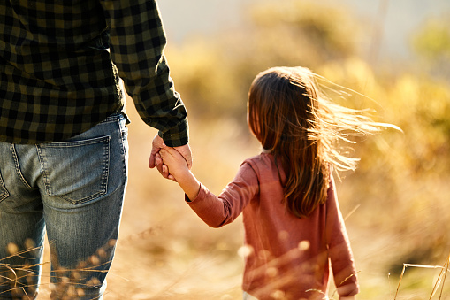 Rear view of a little girl holding hands with her father while spending an autumn day in a meadow.
