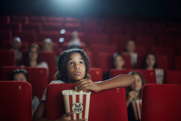 Black girl watching a suspenseful movie in cinema. African American girl eating popcorn while watching a movie projection in cinema. suspenseful stock pictures, royalty-free photos & images