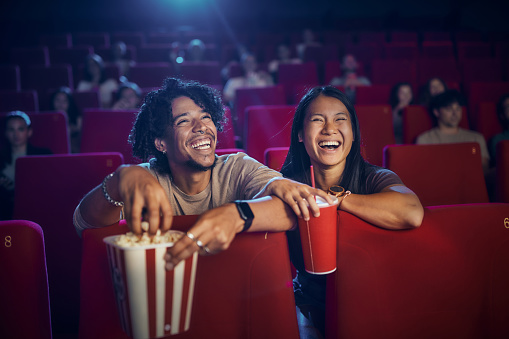 Happy diverse couple enjoying in their snack and drink while watching a movie in theatre.