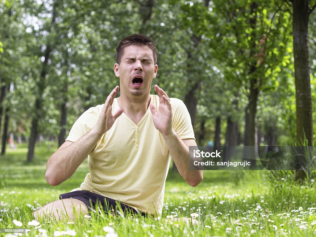 An allergic man sitting in a field with flowers sneezing Young male sneezing outdoors, having problem with allergy Sneezing Stock Photo