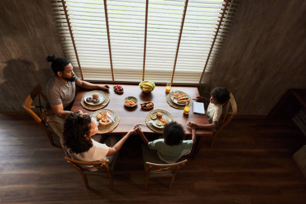 Above view of a black family praying before a meal in dining room.