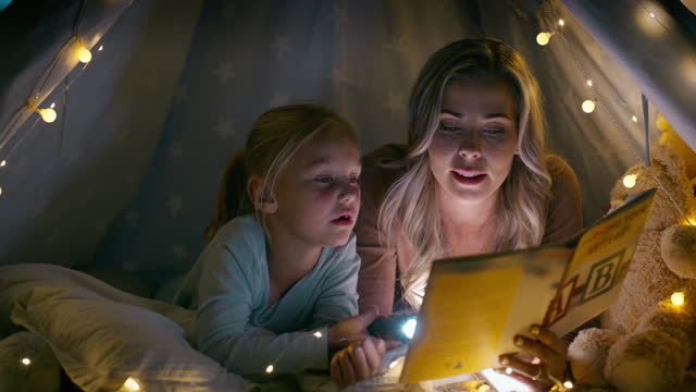 Woman, child and reading in dark, bedroom and lights for learning, education and knowledge for growth. Mother, daughter and together with love, care of bonding for future, milestone or development