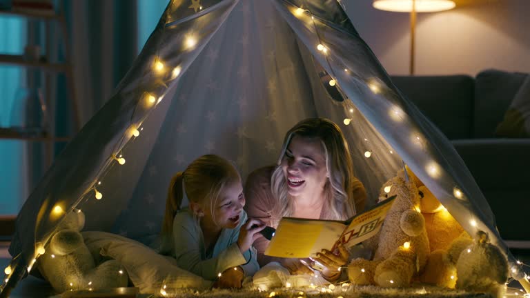Mother, daughter and tent with flashlight for reading, storytelling and story for bonding in living room. Family, woman and girl child with fort on floor of lounge for conversation, love and happy