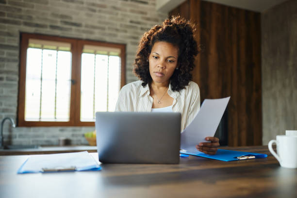 istock Young black woman working on documents and laptop at home. 1805403466