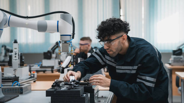 student engineer assembling robotic arm with computer in technology workshop. service engineer holding robot controller and checking robotic arm welding hardware. - stem stockfoto's en -beelden