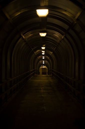 Wide angle color image depicting the diminishing perspective of a illuminated metal tunnel on the London underground network. There are no people around, and the tunnel leads to London tube train in the distance. Room for copy space.