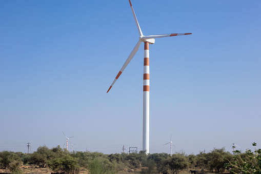 Number of wind mills painted in red and white standing on clear blue sky background to generate electric power