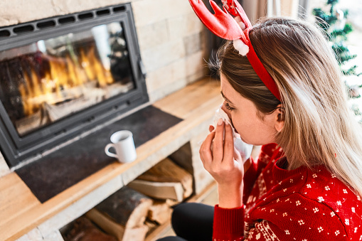 Young woman with a common cold in living room on Christmas day blowing nose