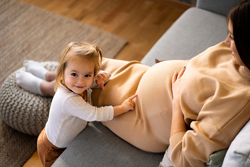 Excited little girl touching her pregnant mother's belly while resting at home