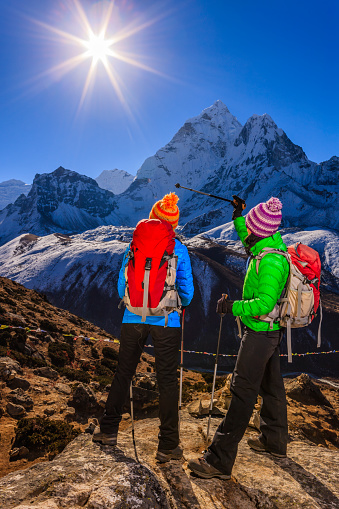 Two young women standing on the top of a mountain and watching sunrise over Himalayas  The sun and mount Ama Dablam on a background. Mount Everest National Park. This is the highest national park in the world, with the entire park located above 3,000 m ( 9,700 ft). This park includes three peaks higher than 8,000 m, including Mt Everest.