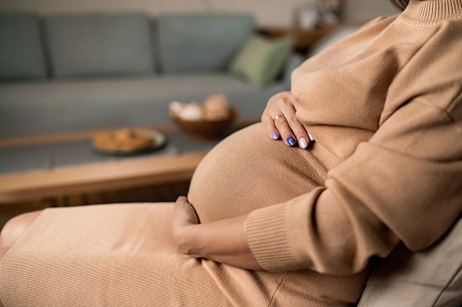 Close-up of unrecognizable pregnant woman touching her belly while sitting at home