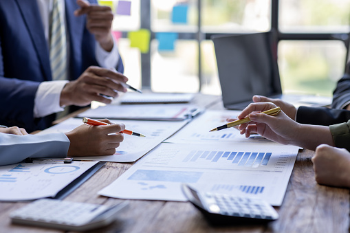 Group of confident business people point to graphs and charts to analyze market data, balance sheet, account, net profit to plan new sales strategies to increase production capacity.