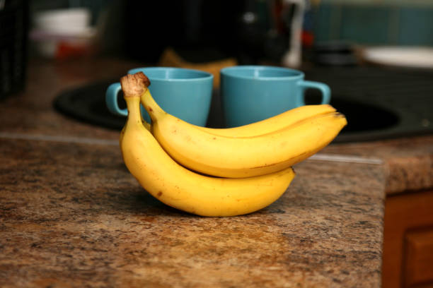 istock A bunch of bananas lying on a solid kitchen table. Sweet ripe bananas with yellow skin. Kitchen Scene with Bananas and Mixed Fruits Hand of ripe bananas in kitchen countertop 1805481977