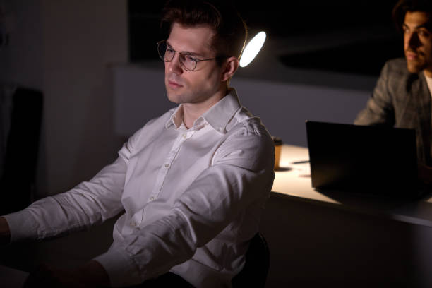 istock Caucasian focused young man working remotely late at night in office using computer 1805494025