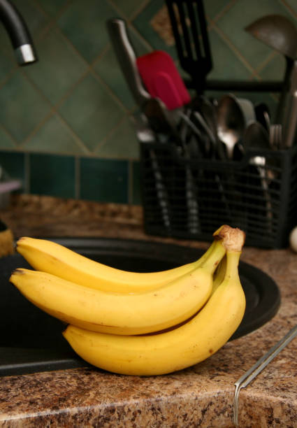 istock A bunch of bananas lying on a solid kitchen table. Sweet ripe bananas with yellow skin. Kitchen Scene with Bananas and Mixed Fruits Hand of ripe bananas in kitchen countertop 1805511370