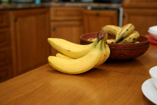 istock A bunch of bananas lying on a solid kitchen table. Sweet ripe bananas with yellow skin. Kitchen Scene with Bananas and Mixed Fruits Hand of ripe bananas in kitchen countertop 1805513069