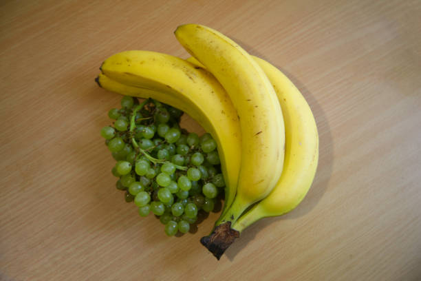 A bunch of bananas lying on a solid kitchen table. Sweet ripe bananas with yellow skin. Kitchen Scene with Bananas and Mixed Fruits Hand of ripe bananas in kitchen countertop