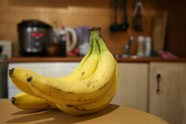 istock A bunch of bananas lying on a solid kitchen table. Sweet ripe bananas with yellow skin. Kitchen Scene with Bananas and Mixed Fruits Hand of ripe bananas in kitchen countertop 1805515702