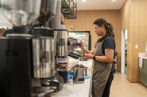 A female barista stands at her work station making coffee