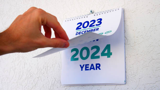 Close-up of a male hand flipping through the December page of 2023 wall calendar followed by the title page of a new 2024 calendar stock photo