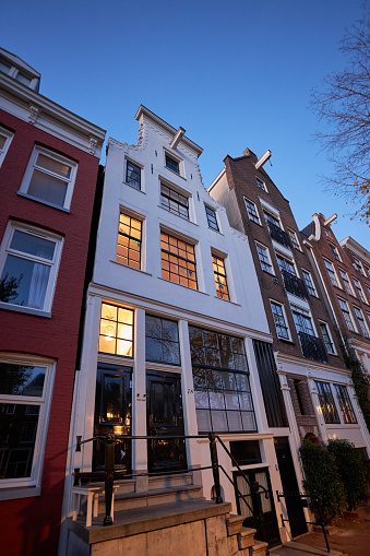 City street with white canal house at dusk in Amsterdam, The Netherlands.