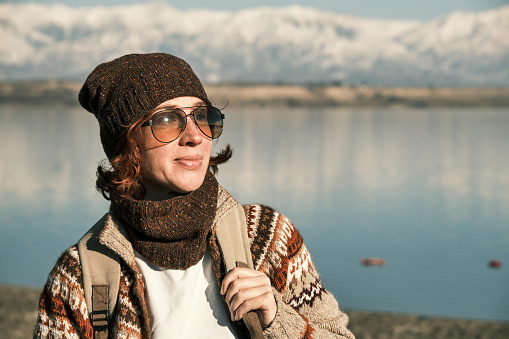 Portrait of cheerful 45-year-old female hiker on high lake shore  with snowcapped mountain ridge on horizon
