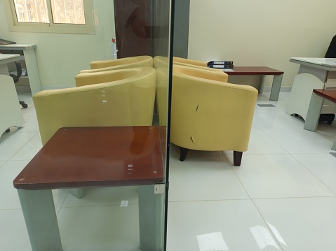 Two pairs of orange leather chairs separated by a glass partition in two adjacent offices, 3 brown tables, 2 desks